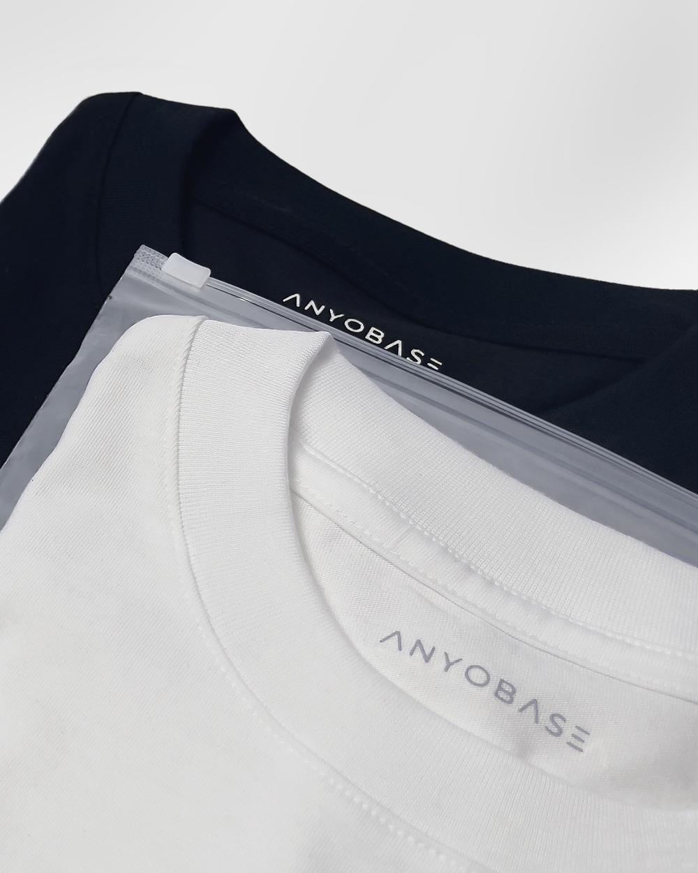 ANYOBASE Core Tee in Black and Off-White displayed in frosted zip polybags.
