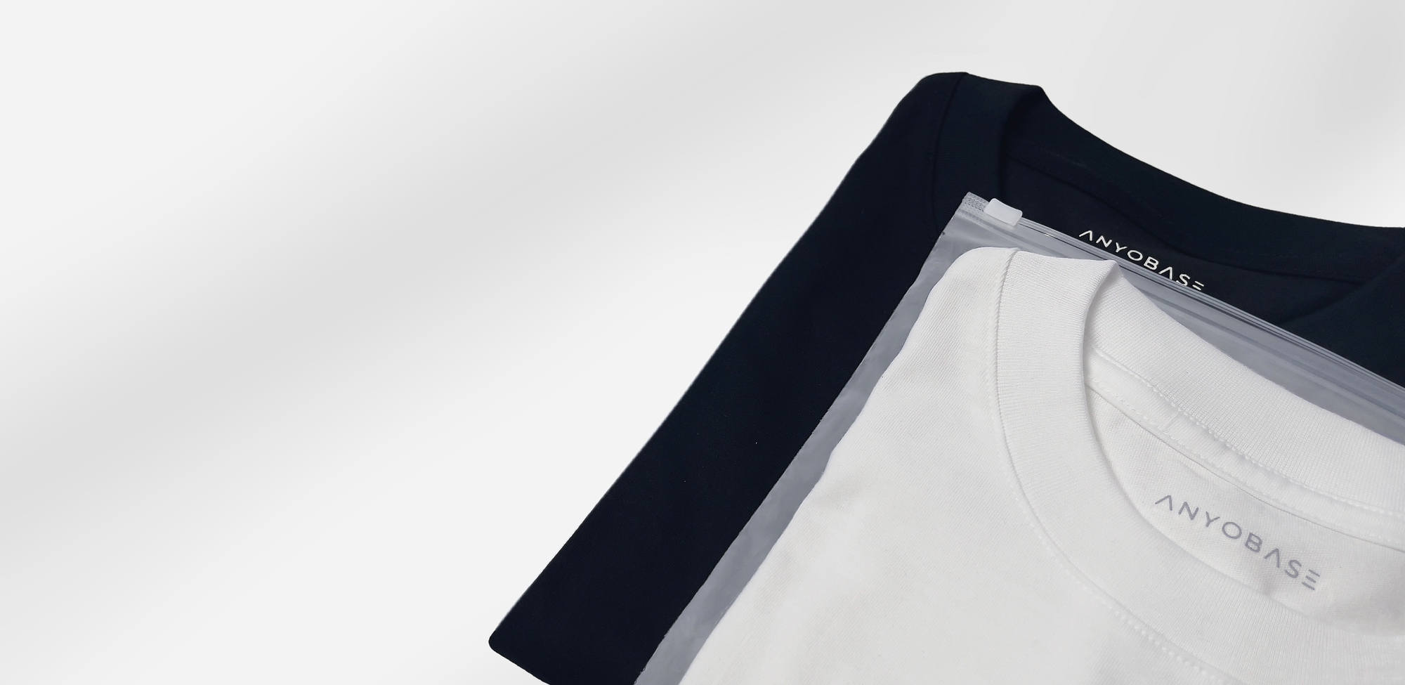 ANYOBASE Core Tee in Black and Off-White displayed in frosted zip polybags.